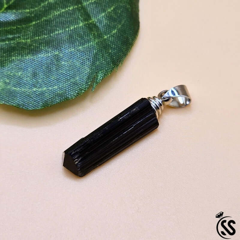 Black Tourmaline real stone pendant on a leaf, known for protection and energy grounding.
