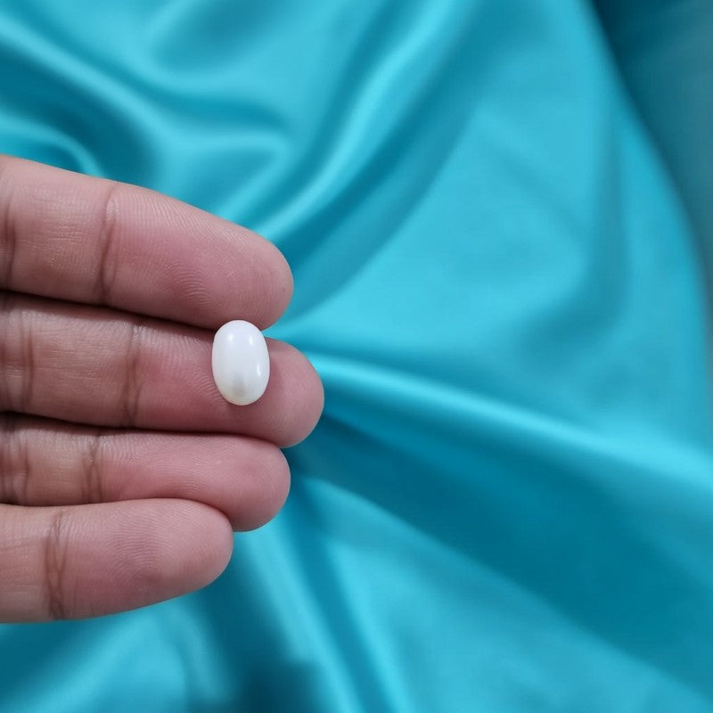 SilverStones.Pk 3 carat natural white Marjan coral gemstone held between fingers against a blue satin background