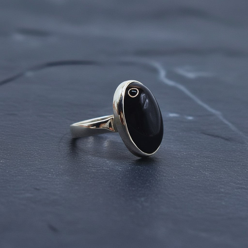 SilverStones.Pk handmade oval black aqeeq gemstone ring with silver band. A sprig of purple flowers is in the background.