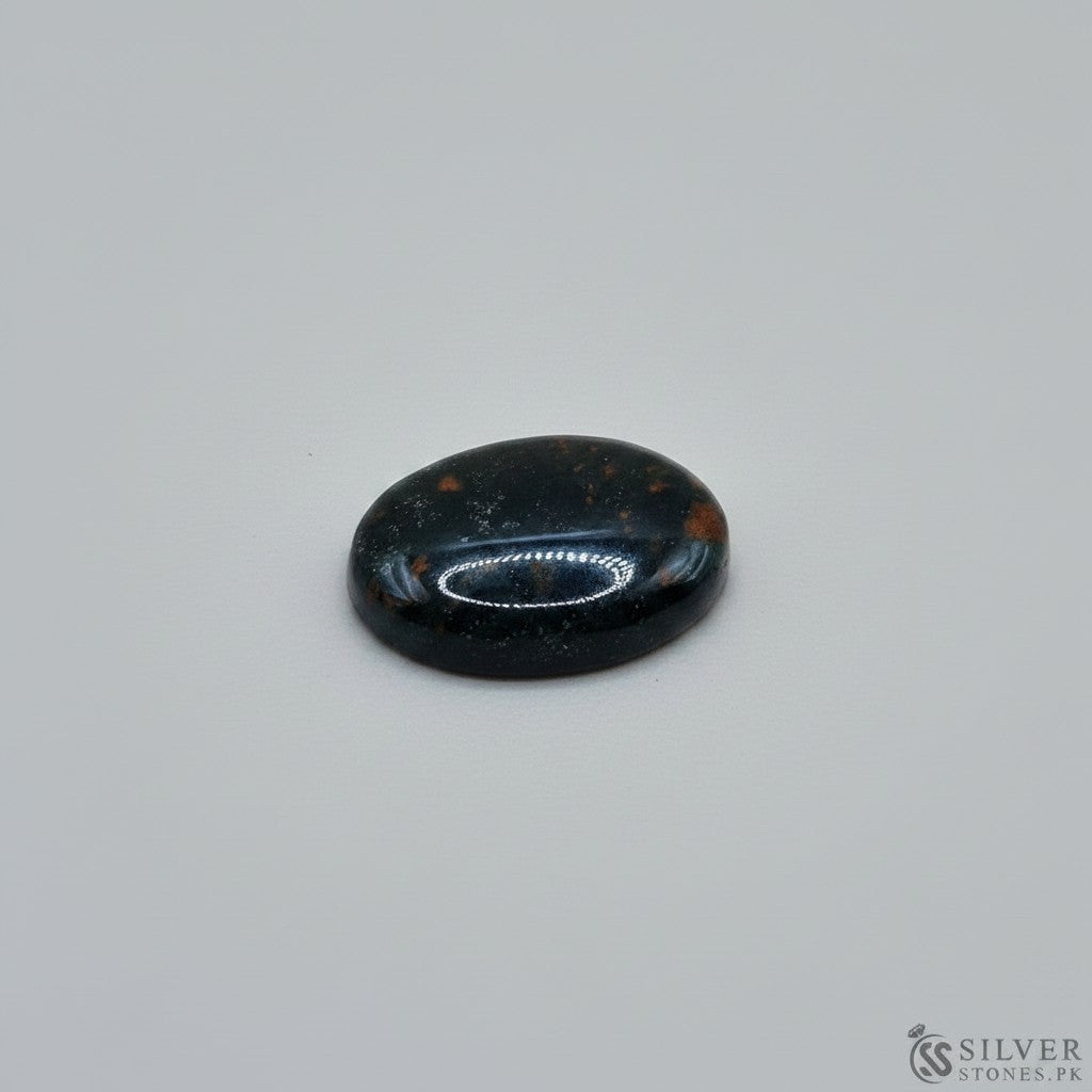 SilverStones.Pk oval cabochon bloodstone gemstone with red inclusions on a light wood background.