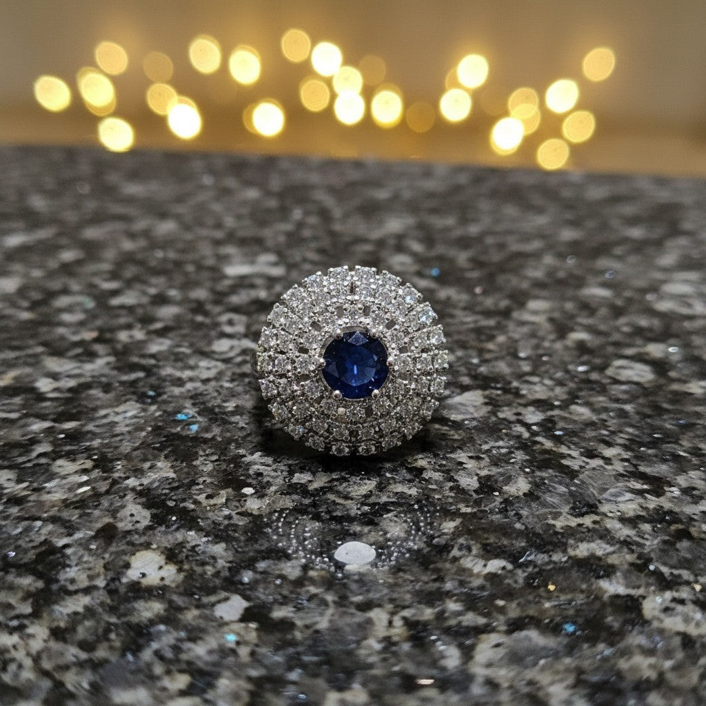 SilverStones.Pk imitation ladies ring with a central blue zircon stone surrounded by small clear zircon stones, set in silver-tone metal.