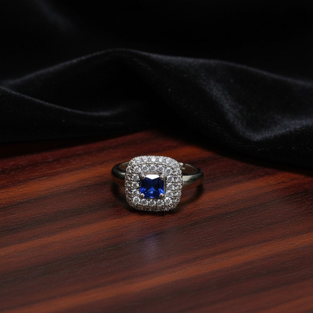 SilverStones.Pk adjustable ring with a central blue zircon stone surrounded by small clear zircon stones in a square halo setting.