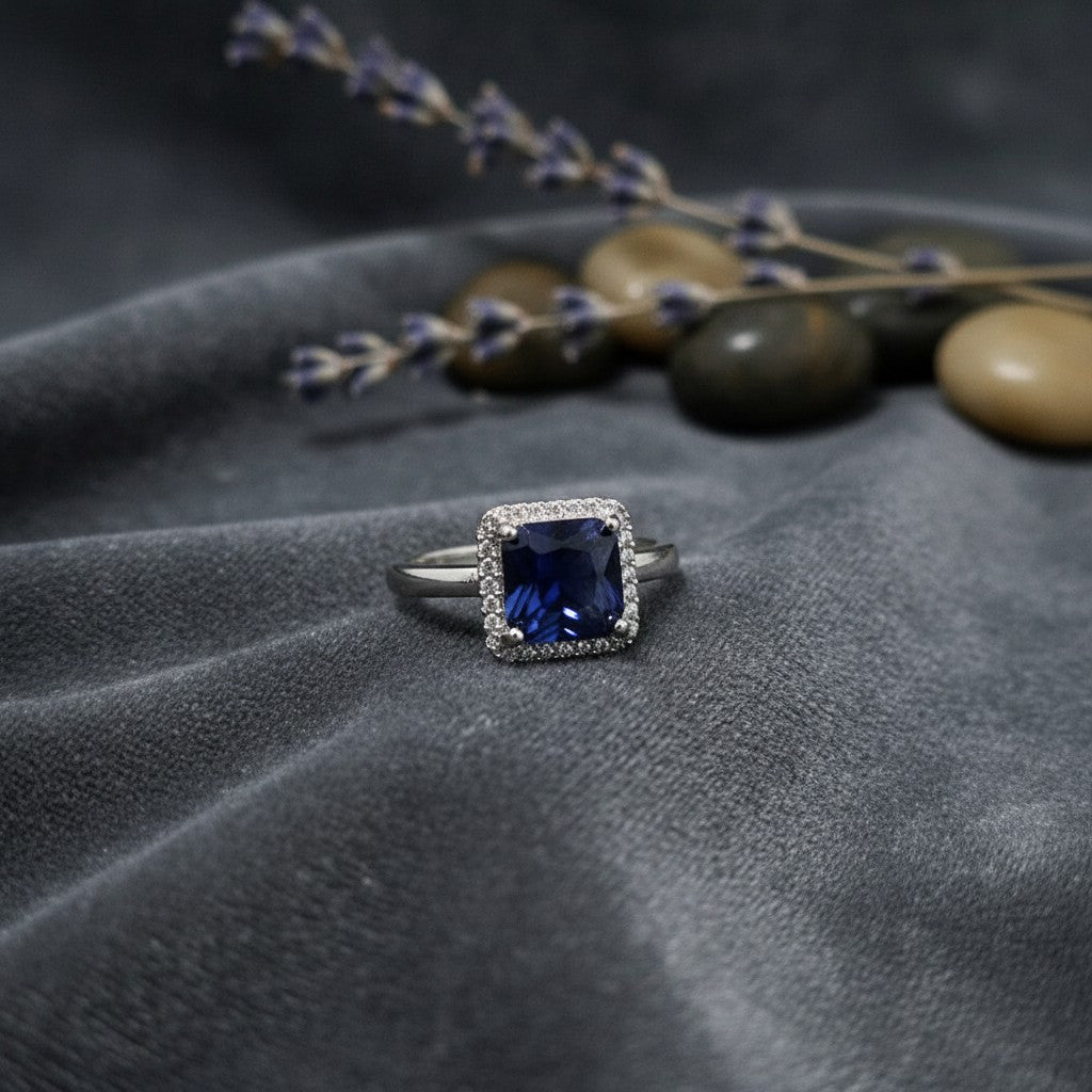 SilverStones.Pk imitation ring with a deep blue square zircon stone surrounded by small clear stones, set in silver-tone metal.