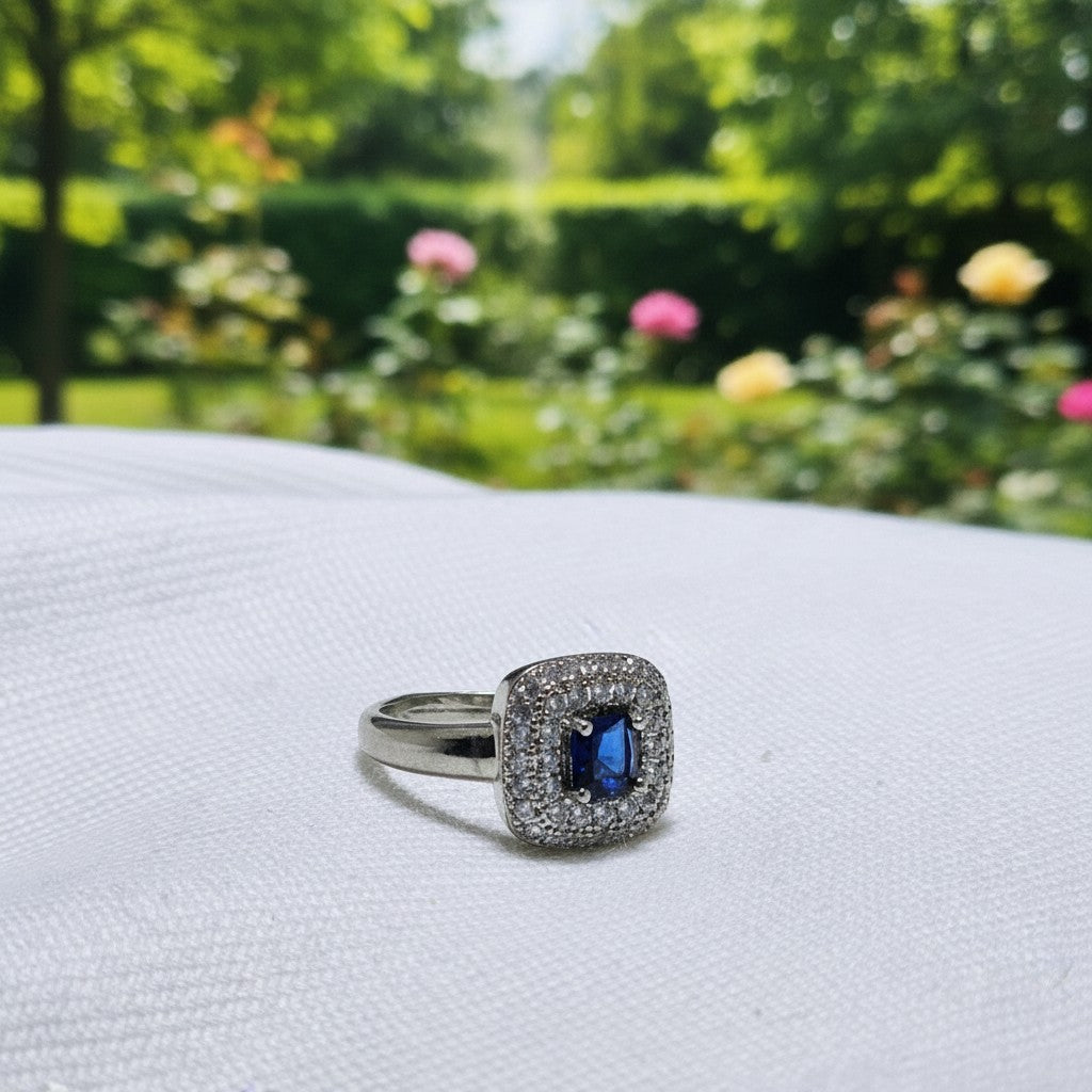 SilverStones.Pk ladies ring with a central blue zircon stone surrounded by small clear zircon stones, set in silver-tone metal.