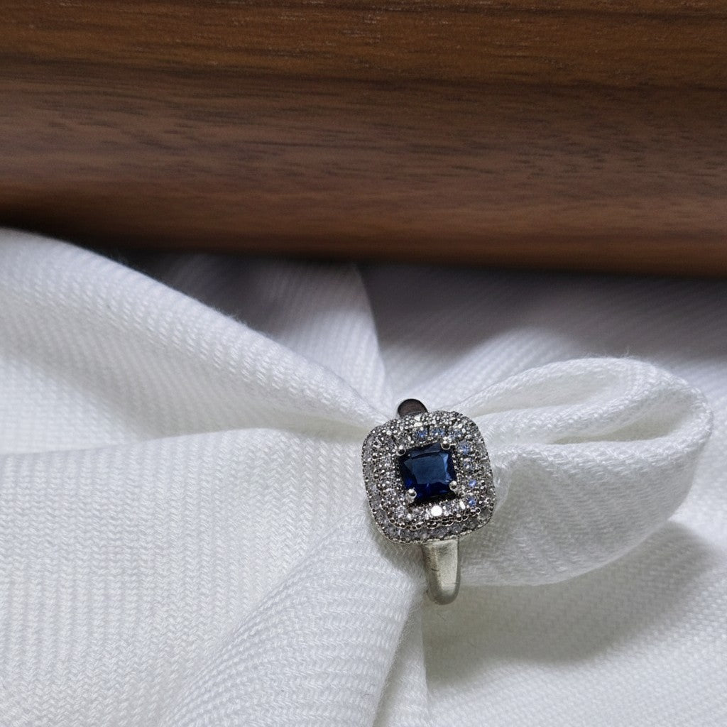 SilverStones.Pk designer ladies ring with a central dark blue zircon stone surrounded by smaller clear zircon stones, set in silver-tone metal.