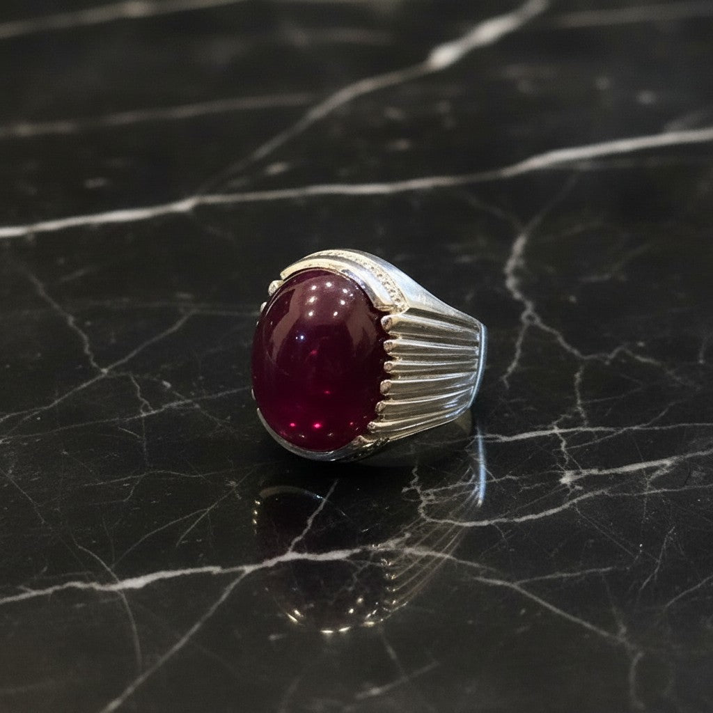 SilverStones.Pk men's silver ring with a large, oval, deep red Irani Yaqoot (ruby) stone and small accent stones. Features a ribbed band design.