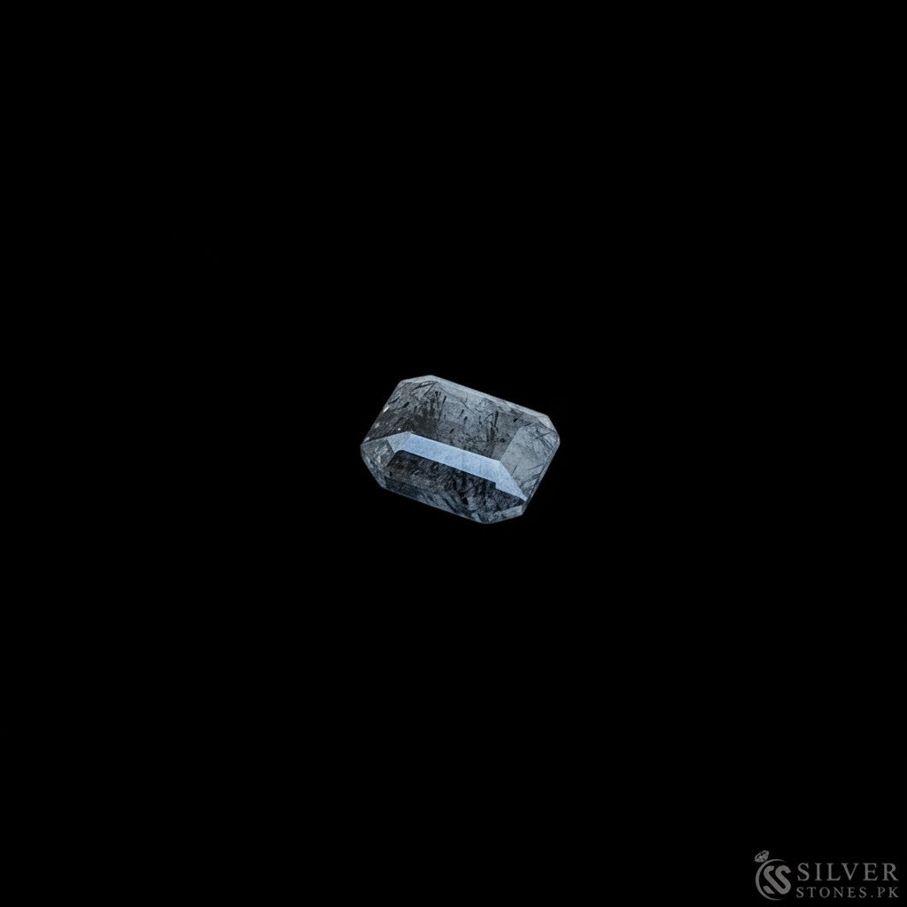 SilverStones.Pk real Muh-e-Najaf stone, faceted rectangular shape, dark grey with natural inclusions, on a light wood background.