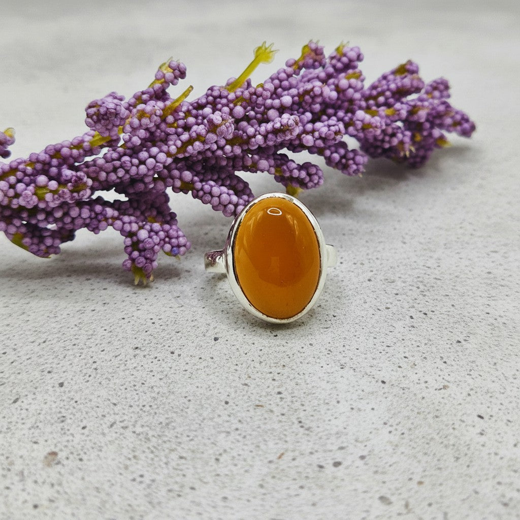 SilverStones.Pk handmade oval orange Aqeeq gemstone ring set in silver. A sprig of purple flowers rests behind the ring.