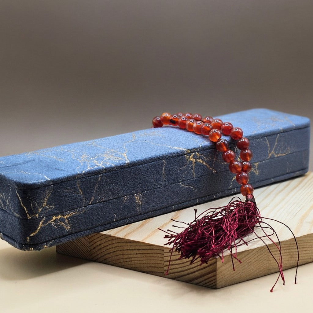 Silverstones.Pk real aqeeq stone tasbeeh with red tassel. Orange-red polished beads on a dark blue textured box.