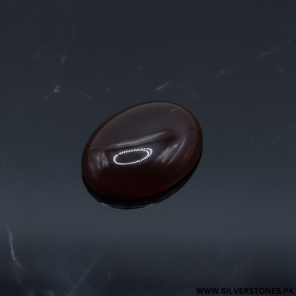 SilverStones.Pk oval-cut real Sulemani Aqeeq stone, deep brown with natural banding, on a light wood background.