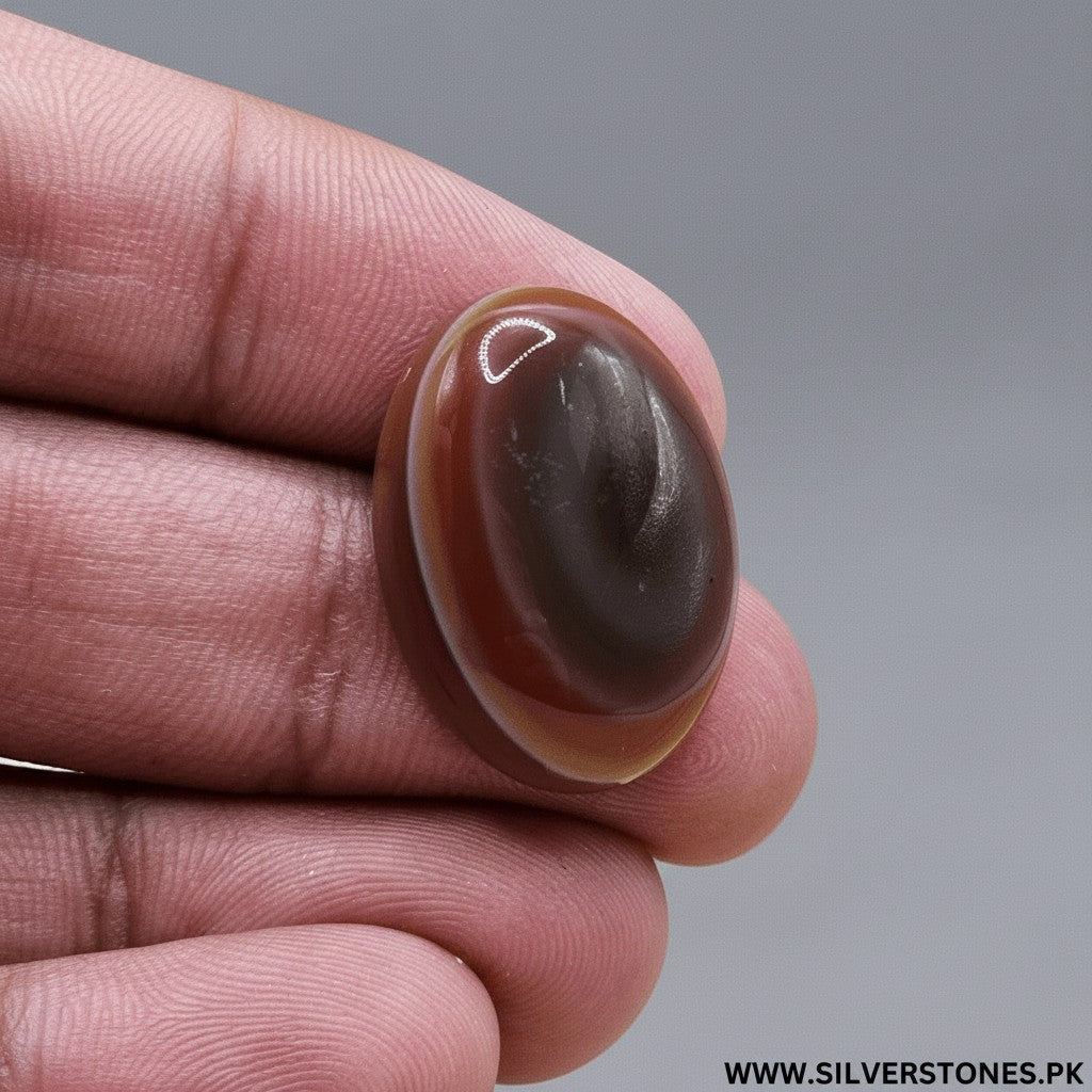 SilverStones.Pk oval Sulemani Aqeeq stone with bands of brown, red, and yellow, held by fingers.
