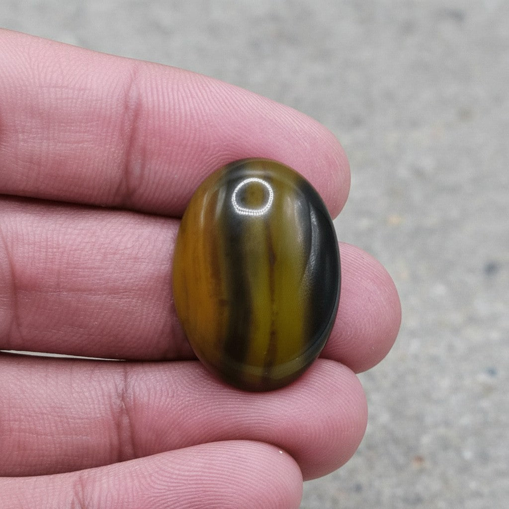 SilverStones.Pk oval Sulemani Aqeeq stone with natural brown and green banding, held in hand.