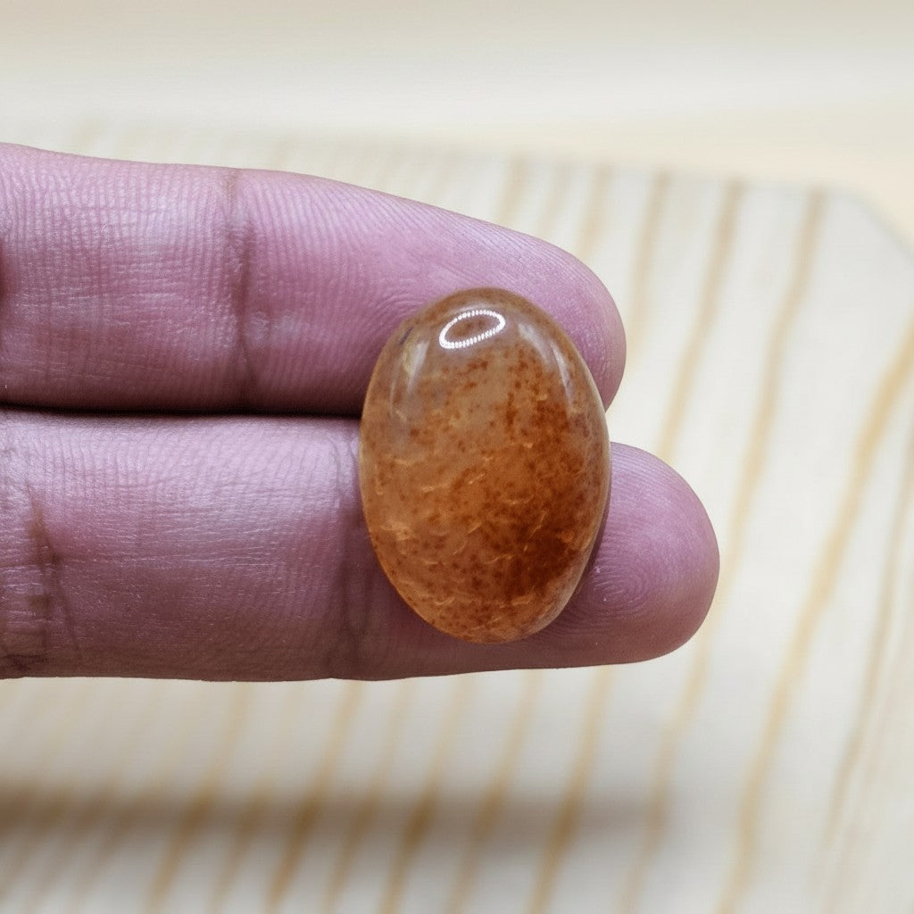 SilverStones.Pk oval-cut real Sulemani Aqeeq stone with warm brown and orange banding, held by fingers.