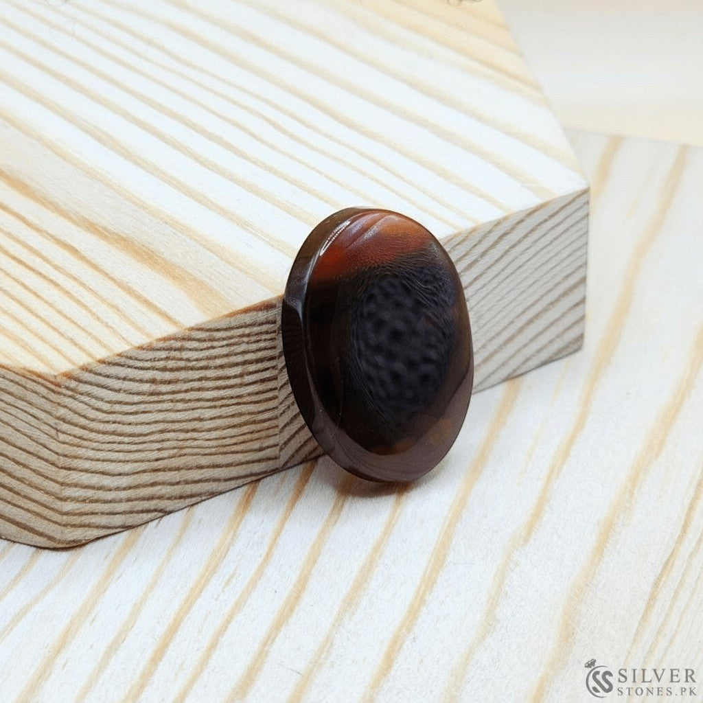 SilverStones.Pk oval Sulemani Aqeeq stone with rich brown and red banding, set on wood.