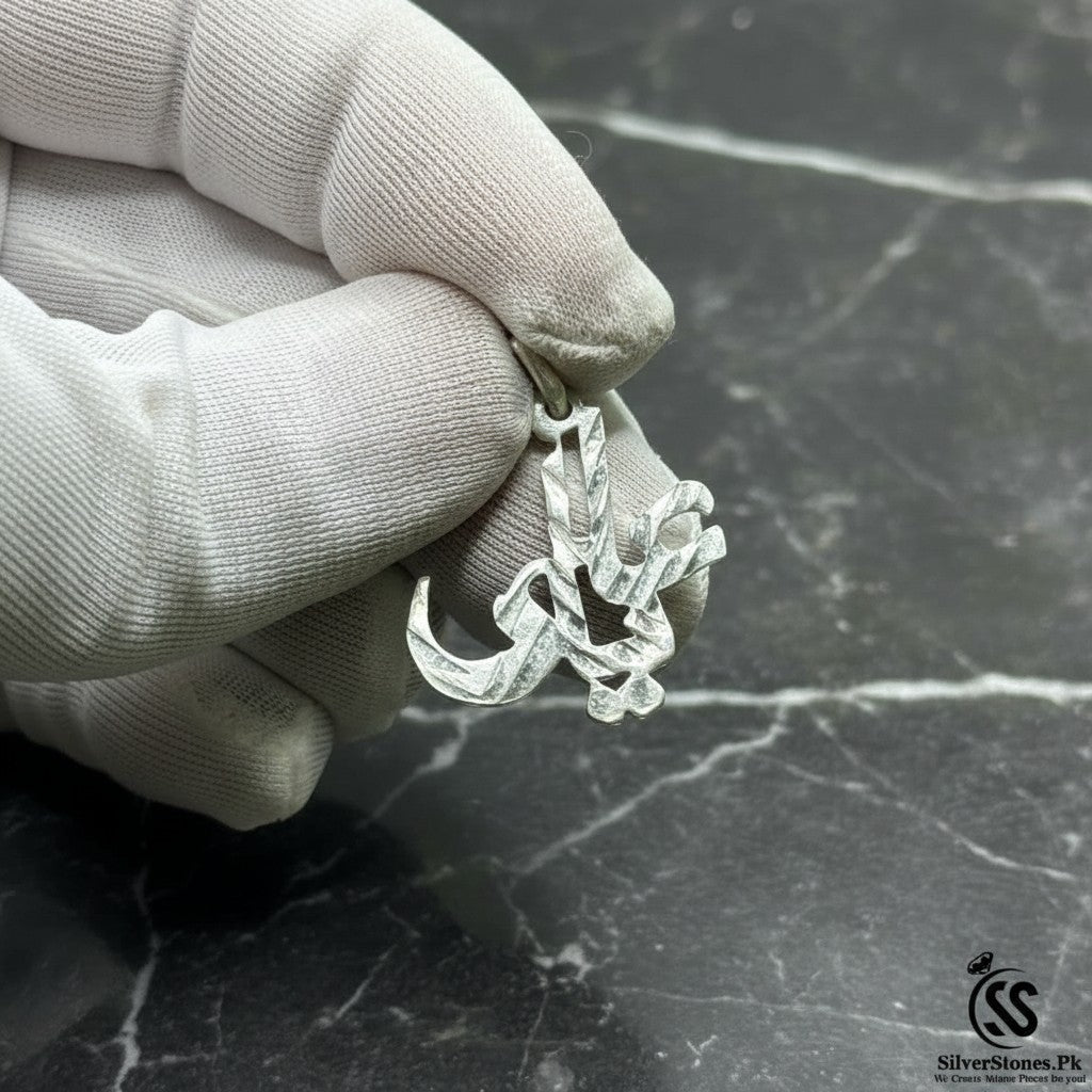 SilverStones.Pk Ya Ali pendant in sterling silver, featuring Arabic calligraphy. Held by a gloved hand against a green grass background.