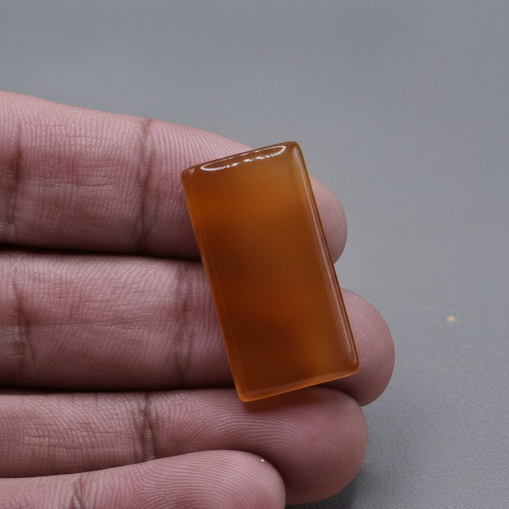 SilverStones.Pk real Yamni Aqeeq stone, rectangular cabochon, translucent orange-brown color, held in hand.